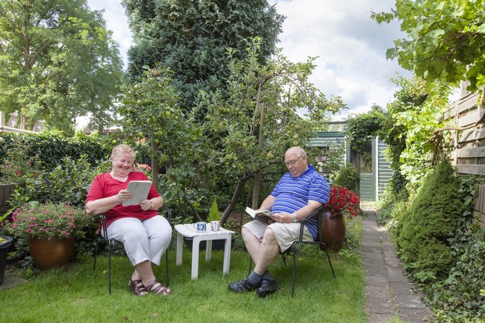 Twee mensen zitten in een groene, koele tuin te lezen.