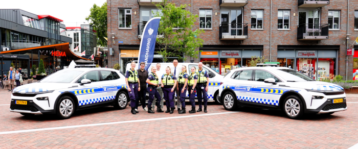 Foto van team handhaving en de burgemeester van Hardenberg. Zij staan op het Marktplein voor de 3 elektrische voertuigen die zij nu hebben: 1 bus en 2 auto's.